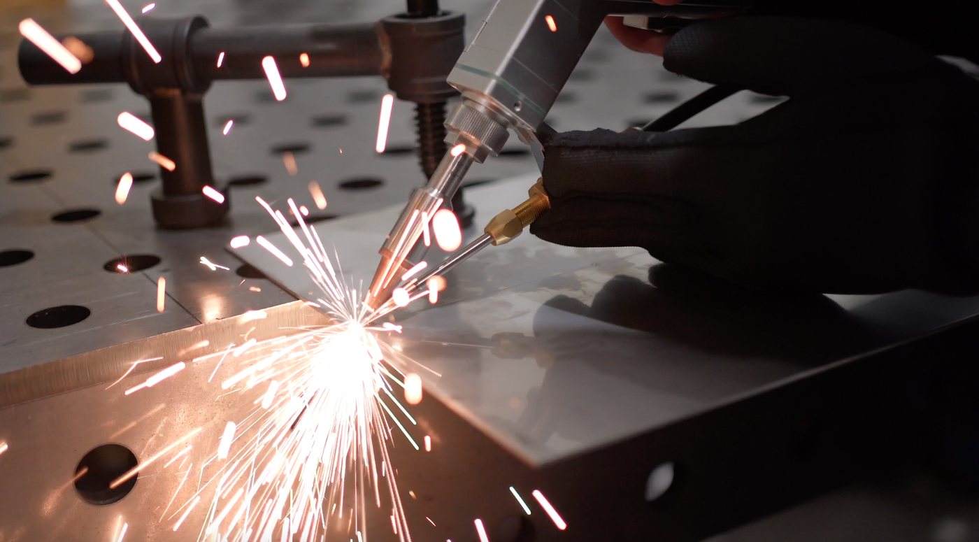 Handlaser beim Schweißen einer Blechkante auf dem Spanntisch, mit Funkenflug