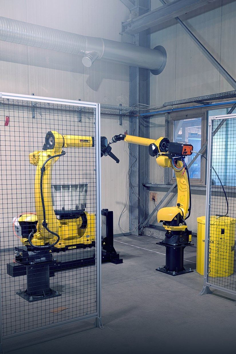 Zwei Fanuc ArcMate 120 Schweißroboter mit Positionierern hinter dem Schutzzaun