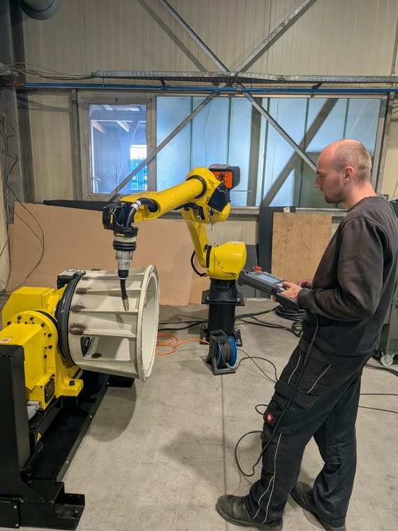 Fanuc ArcMate 120 über einem Rundbauteil auf dem Zweiachs-Positionierer, daneben die Bedienung am Handgerät